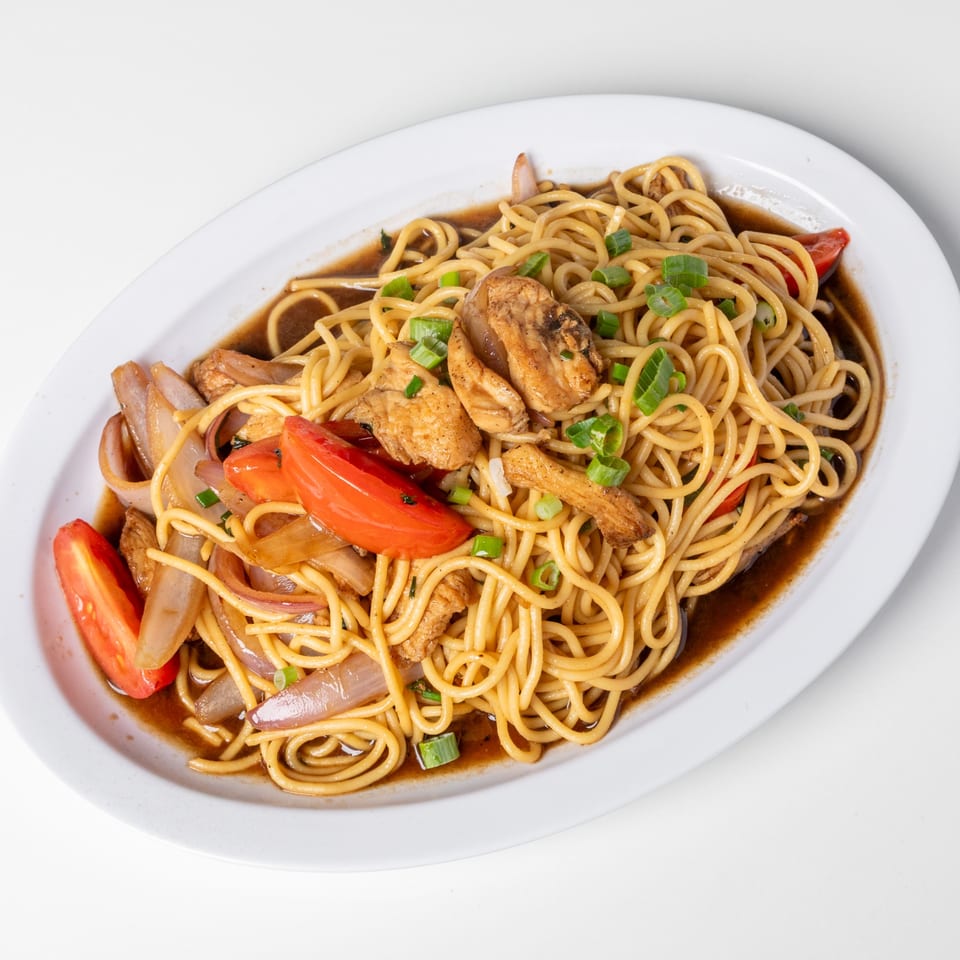 Lomo Saltado with spaghetti, chicken, red onions, tomatoes, and green onions on a white plate.