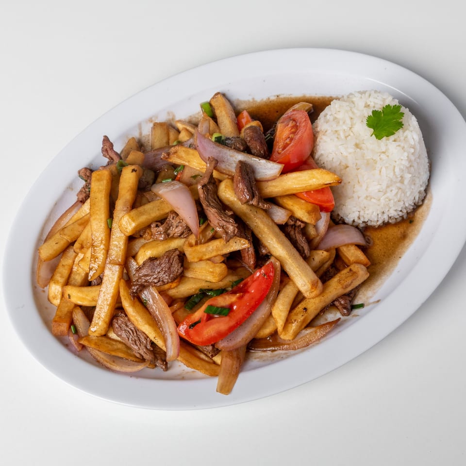 Lomo Saltado with french fries, beef, tomatoes, onions, and rice on a white plate.