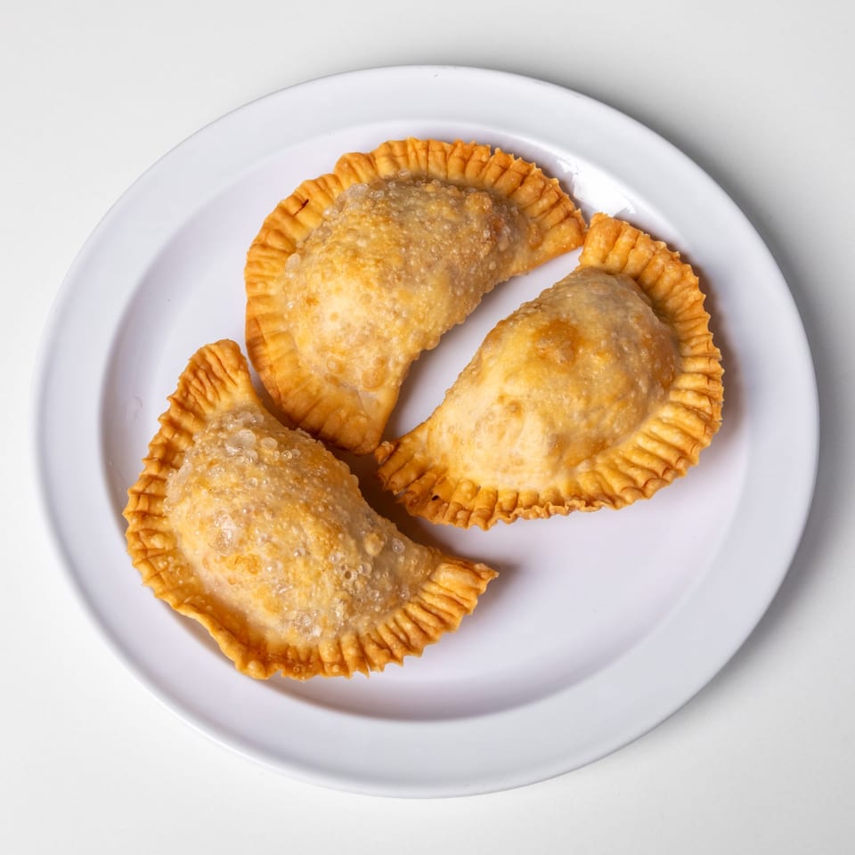 Three golden-brown, fried empanadas with crimped edges are arranged on a white plate.
