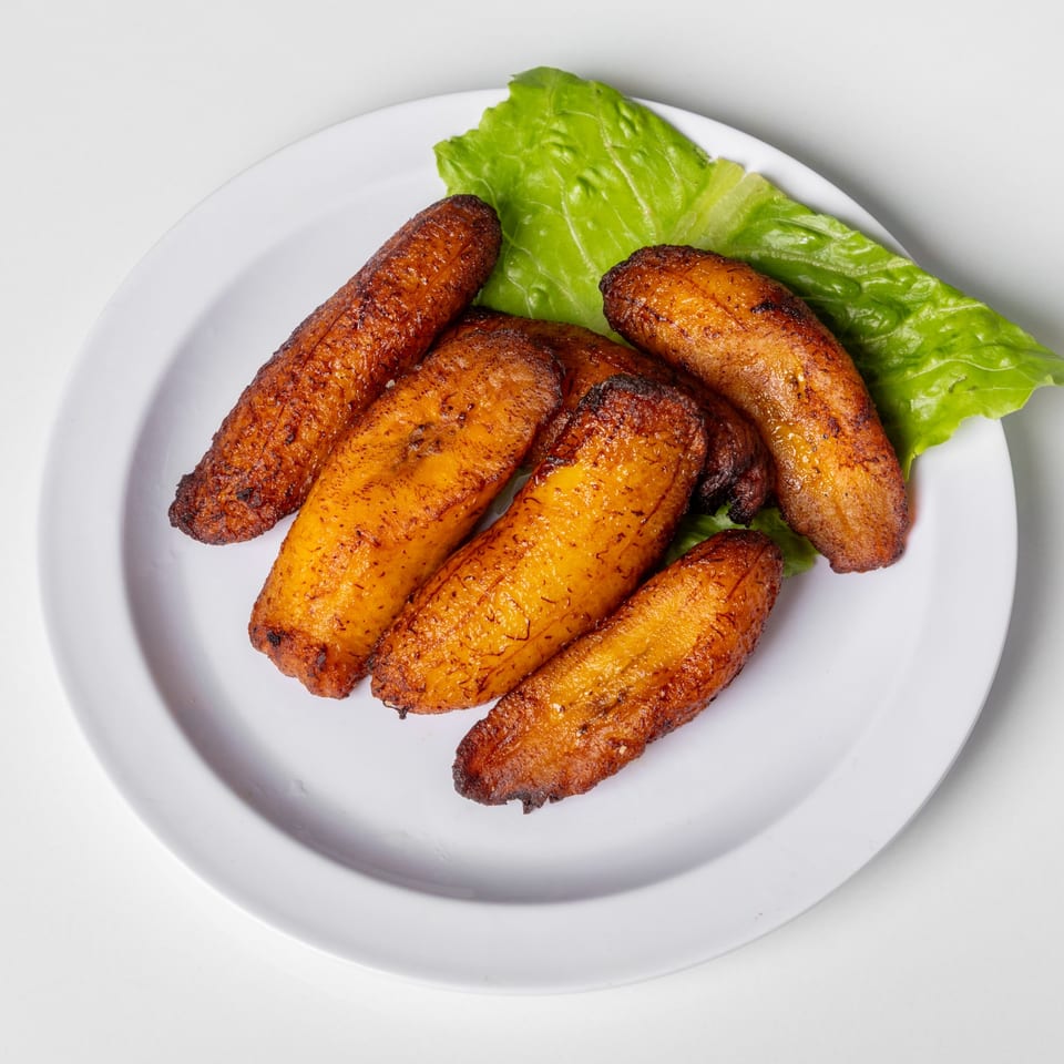 Golden brown fried plantains with a green lettuce leaf on a white plate.