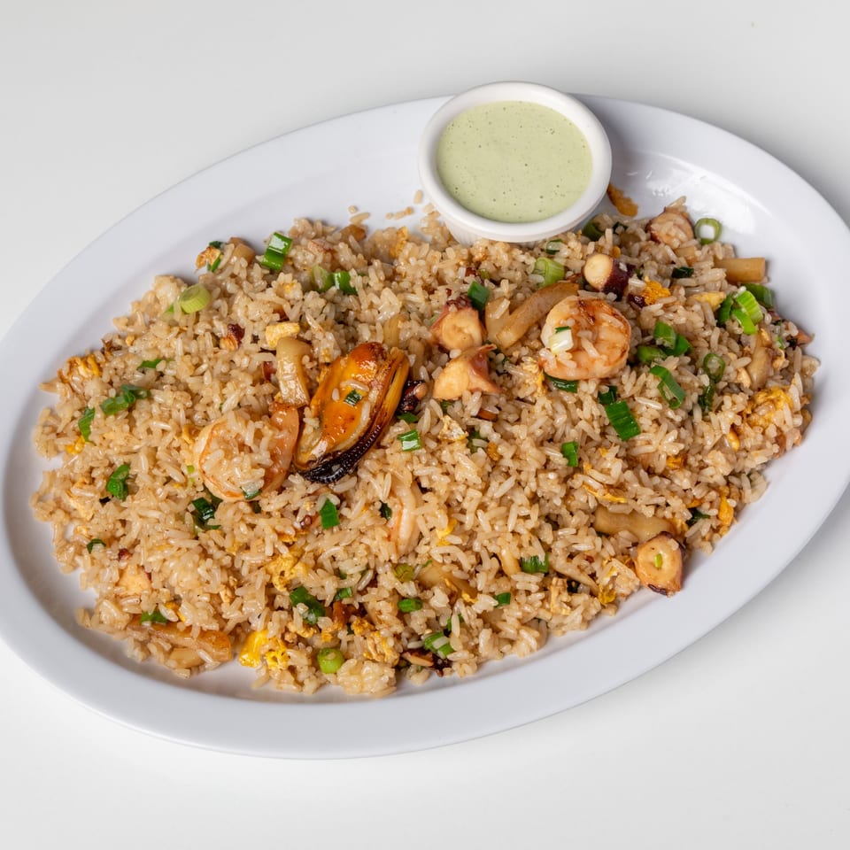 Seafood fried rice with shrimp, mussels, and squid, garnished with green onions and a side of green sauce.